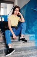 Young teenage girl sitting on stairs of house entrance, wear on yellow t-shirt, jeans and sunglasses.