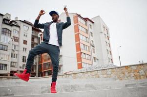 retrato de un hombre afroamericano con estilo saltando en ropa deportiva, gorra y gafas. hombre negro emoción modelo street fashion. foto