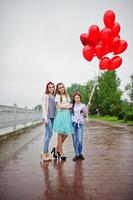 Attractive bride posing with her three lovely bridesmaids with red heart-shaped balloons on the pavement with lake on the background. Bachelorette party. photo