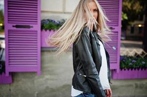 Stylish blonde woman wear at jeans and jacket posed at street against purple window. Fashion urban model portrait. photo
