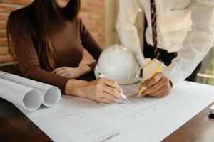 Two colleagues discussing data working and tablet, laptop with on on architectural project at construction site at desk in office photo