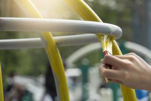 Brush paints a dark yellow paint on it. Oil paint on playground equipment. photo