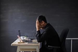 Frustrated and unhappy businessman in suit sitting on office desk with hand on head photo