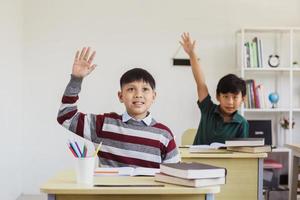 Smart asian elementary students rising their hand in the class for answering teacher question photo