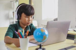 Asian student in headphone writing on paper while looking a laptop photo