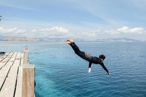 A man in wetsuit jumping into the sea photo