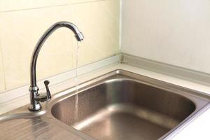 Stainless steel faucet on the sink with water flowing photo