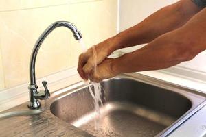 Young man washing his hands with tap water in the kitchen sink. Antivirus and avoiding coronavirus infection.