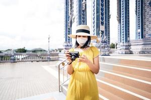 Adult asian woman wear protective face mask for protect virus covid-19 and yellow dress hold camera. photo