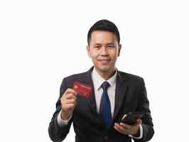 Asian businessman holding red credit card and mobile phone while smiling and online shopping isolated white background. Asian man buy something with credit card shopping online concept. photo
