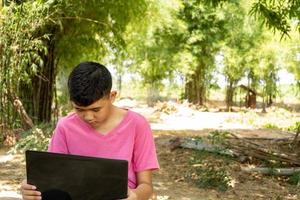 Boy sitting in a chair studying online with laptop computer at home in the countryside photo