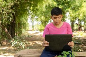 Boy sitting in a chair studying online with laptop computer at home in the countryside photo