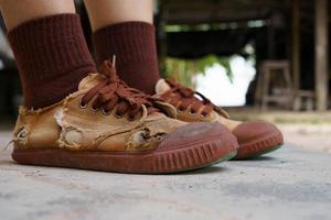 Torn student shoes, Poverty of rural schoolchildren often cannot afford new shoes, high school student legs wearing torn shoes, poor shortage of educational equipment, worn-out brown old sneakers photo