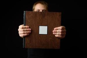 Smiling Man holds Photobooks in a wooden cover on dark background. Copy space photo