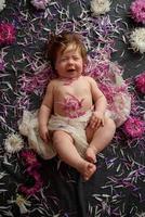 Portrait of a sweet little baby girl with a wreath of flowers on her head indoors photo