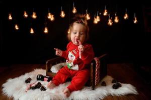 7 month old girl in a red Christmas costume on a background of retro garlands sits on a fur photo