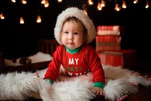 7 month old girl in a red Christmas costume on a background of retro garlands sits on a fur photo