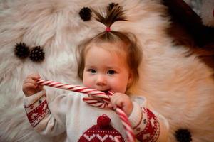 Una niña de 7 meses con un traje rojo de Navidad sobre un fondo de guirnaldas retro se sienta en una piel foto