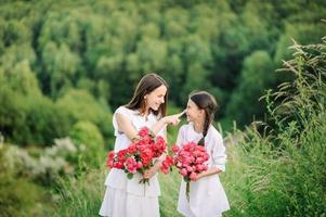 Two sisters dressed in white dresses have fun summertime together. Girls are holding flowers. photo