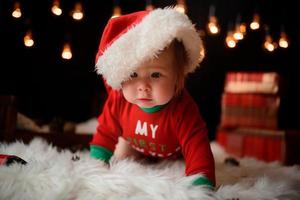 Una niña de 7 meses con un traje rojo de Navidad sobre un fondo de guirnaldas retro se sienta en una piel foto