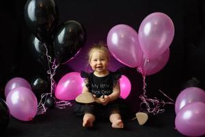 día de la fiesta de cumpleaños de la niña del primer año. globos y vacaciones en interiores. cumpleaños del niño niña bonita en su primer vestido negro foto