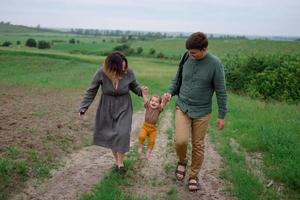 mamá, papá e hija. los padres sostienen al bebé con las manos y van hacia la cámara. foto