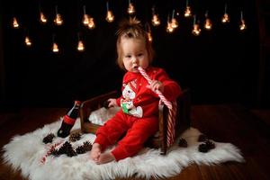 7 month old girl in a red Christmas costume on a background of retro garlands sits on a fur photo