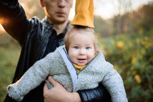 Happy smiling Caucasian father dad with cute adorable baby girl. Family in autumn fall park outdoor with yellow orange leaves trees. photo