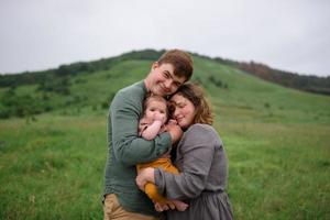 mamá, papá e hija. los padres sostienen al bebé con las manos y van hacia la cámara. foto