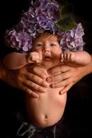 Father's hands are holding a little daughter with hydrangea flowers on her head. Shot on a black background. photo