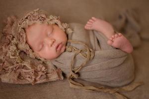 una niña recién nacida duerme en un envoltorio marrón sobre un fondo de tela marrón. foto