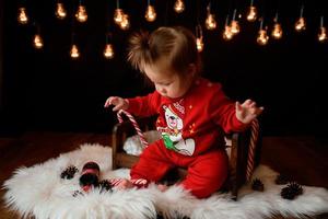 7 month old girl in a red Christmas costume on a background of retro garlands sits on a fur photo