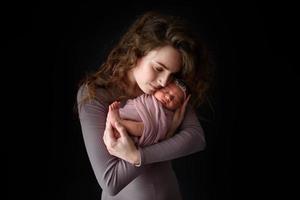 mamá está sosteniendo a su hija recién nacida. foto tomada en un fondo oscuro.