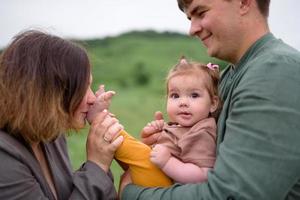 Mom, dad and daughter. Parents Hold baby by hands and go towards the camera. photo