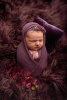 Cute newborn girl sleeping on a purple flocket in a purple wrap.