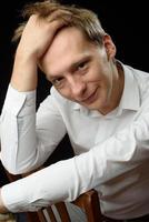 Close up portrait of a young man in a white shirt and black tie, smiling while looking at the camera, against plain studio background photo