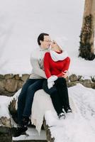 A young lovers couple in winter jackets and scarves sitting in a snow park photo