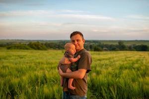 un padre joven sostiene a su hijo de tres meses en sus brazos. filmado en un campo de trigo. foto