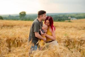 padre, madre y su pequeño hijo se divierten juntos en un campo de trigo. foto