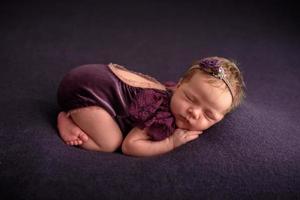 Newborn girl sleeps in a lilac dress on a lilac fabric background photo