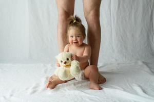 little girl sits happy on a white background and legs of her father photo