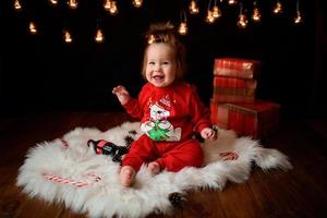 7 month old girl in a red Christmas costume on a background of retro garlands sits on a fur photo