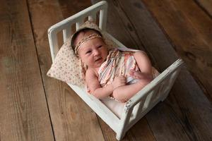 Newborn girl lying on a miniature crib photo