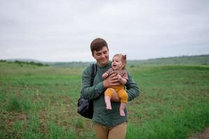 Mom, dad and daughter. Parents Hold baby by hands and go towards the camera. photo