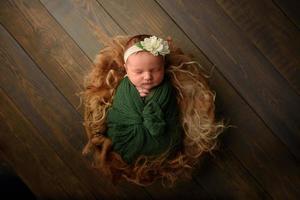 niña recién nacida duerme en una envoltura verde sobre un fondo de madera en piel. foto