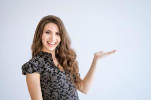 A young beautiful woman smiles on a white background and points to the side photo