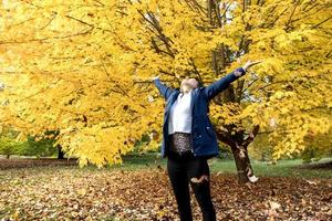 woman stands by a tree and enjoys the leaves falling photo