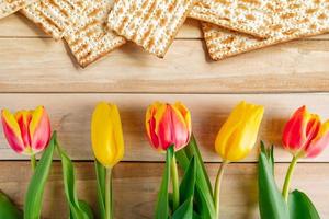 Background Religious Jewish holiday Pesach. Tulips and matzo on a light wooden table. photo