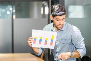 Young businessman holding paper and sitting on table, business team of coworkers meeting in creative office, Teamwork concept photo