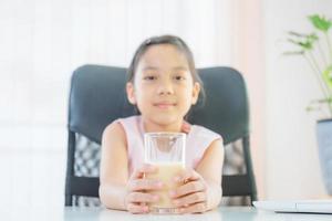 Cheerful little girl smiling and holding glasses of milk, Learn from home concept photo
